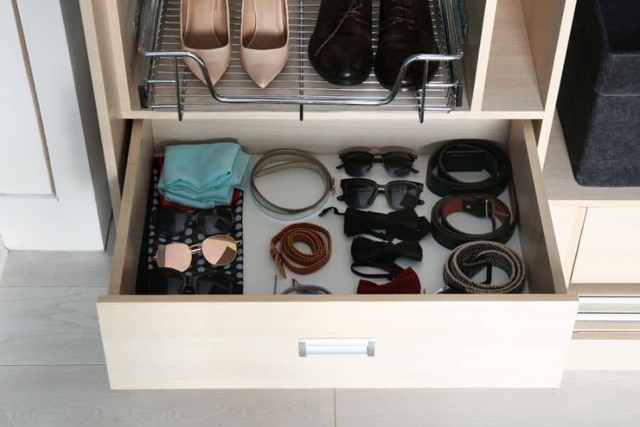 Open drawer with sunglasses, belts, and neckties; above, a rack with two pairs of shoes, beige and brown; neatly organized closet