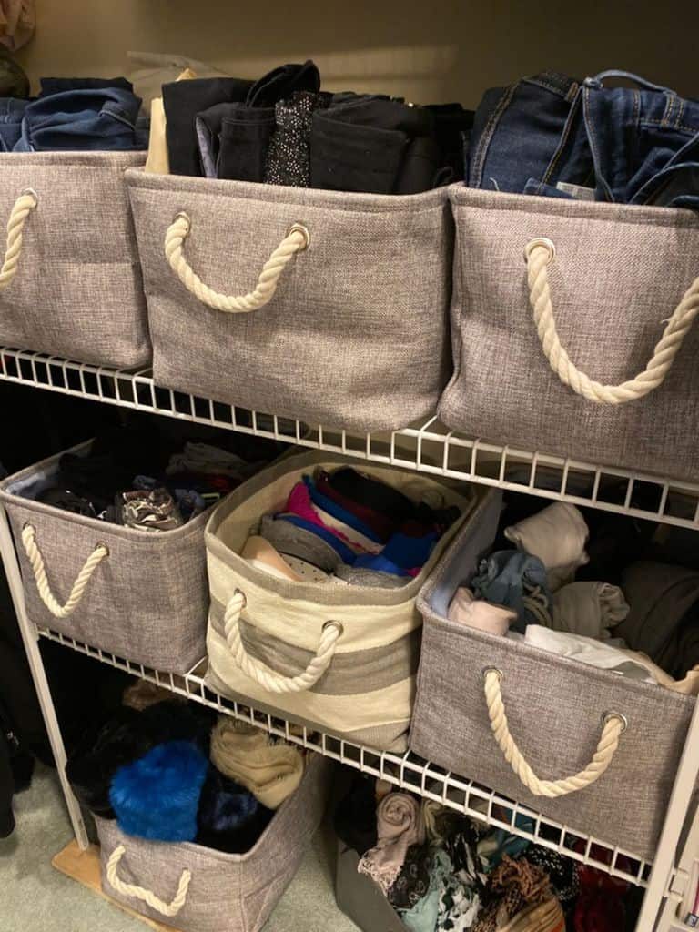 Storage shelves with beige fabric bins filled with folded clothes and accessories, featuring rope handles for easy access