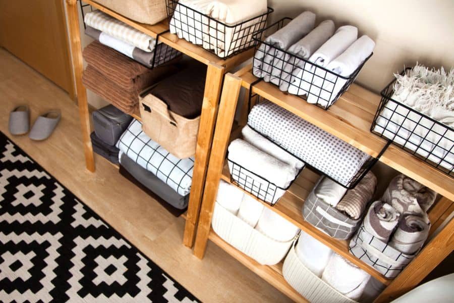 Neatly organized shelves with folded towels and baskets, black and white patterned rug and slippers on the wooden floor