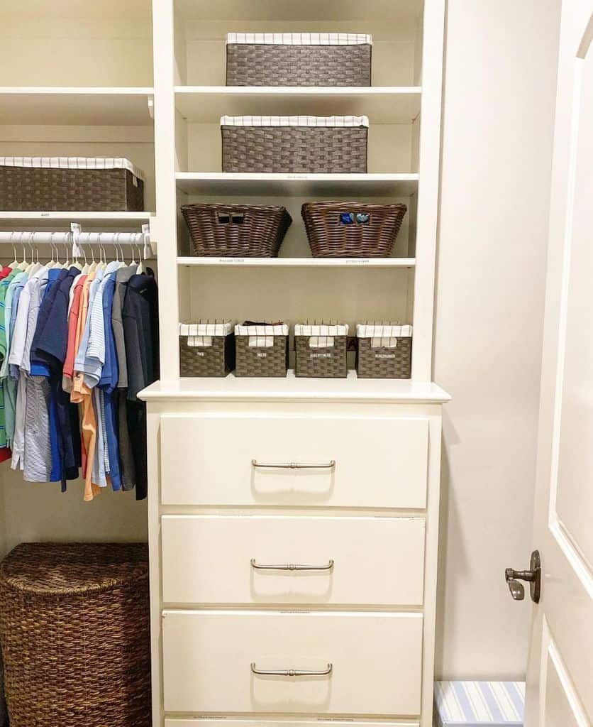 A tidy closet with organized shelves, labeled baskets, a row of shirts on hangers, a tall drawer unit, and a woven laundry basket