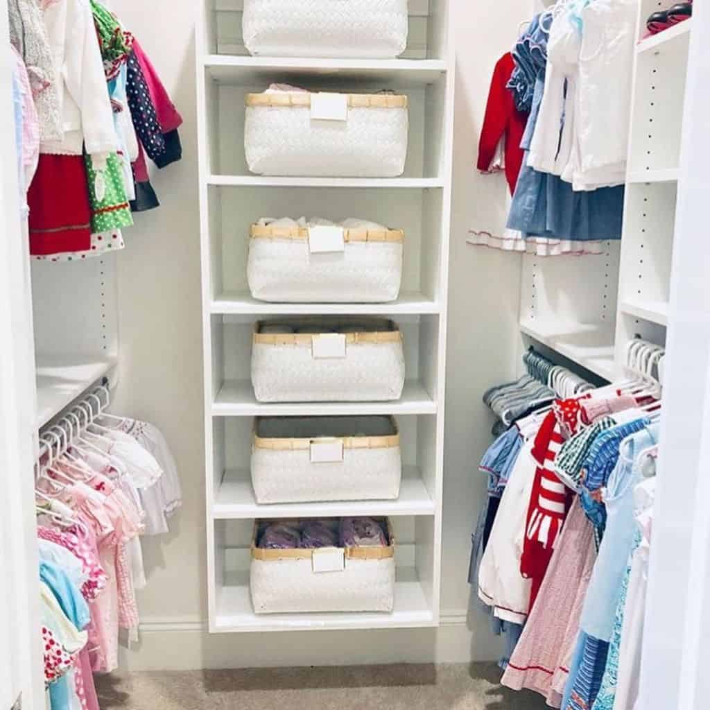 Children's closet with neatly arranged clothes and five white storage baskets on shelves in the center