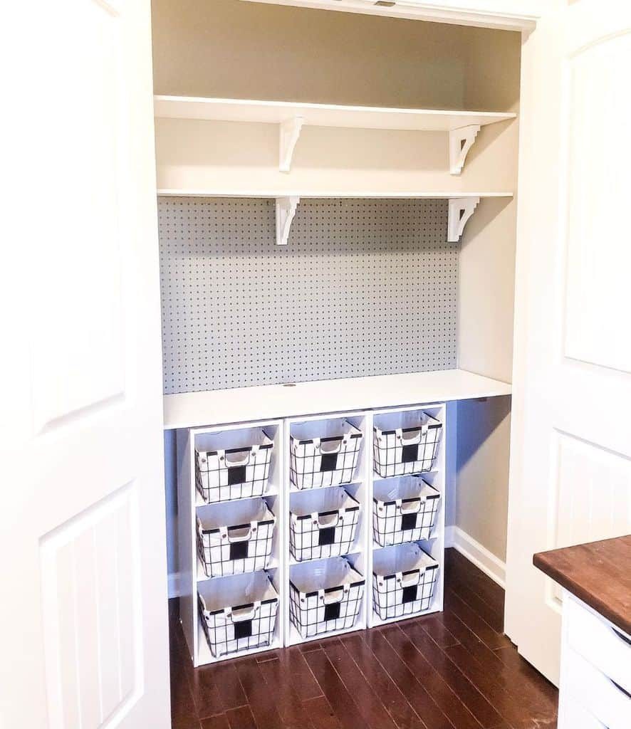 Closet with white shelving, a grey pegboard, and nine cubbies holding white and black wire baskets, dark wooden floor