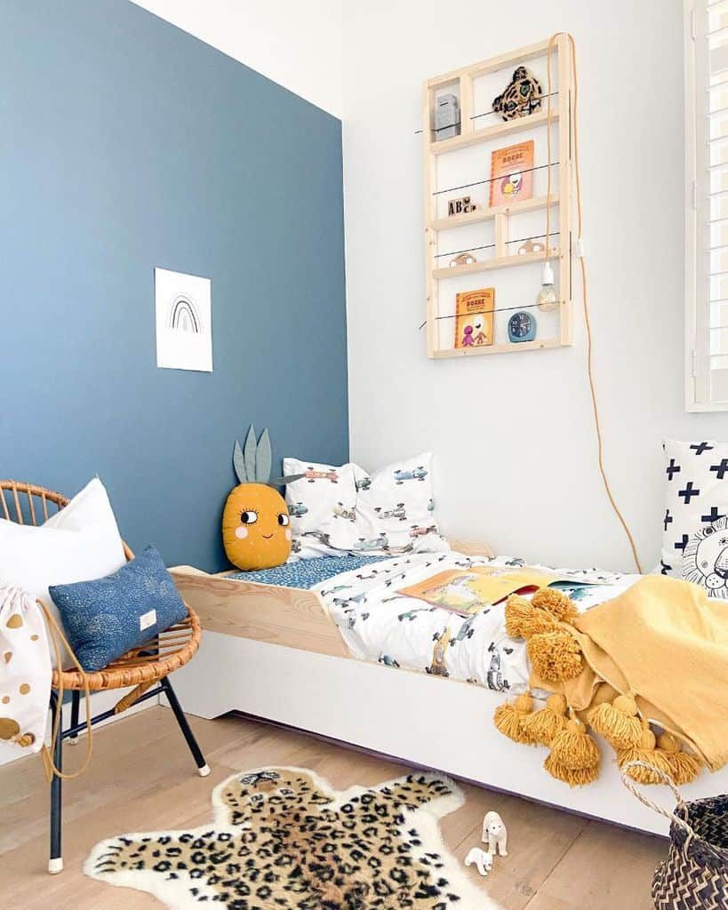 Stylish kids' room with a blue accent wall, cozy wooden bed, playful pineapple pillow, wall-mounted bookshelf, and a leopard rug