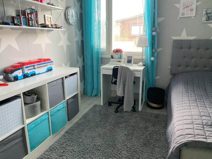 Modern kids' room with star-patterned walls, teal curtains, a study desk, cozy storage bins, and a gray upholstered bed