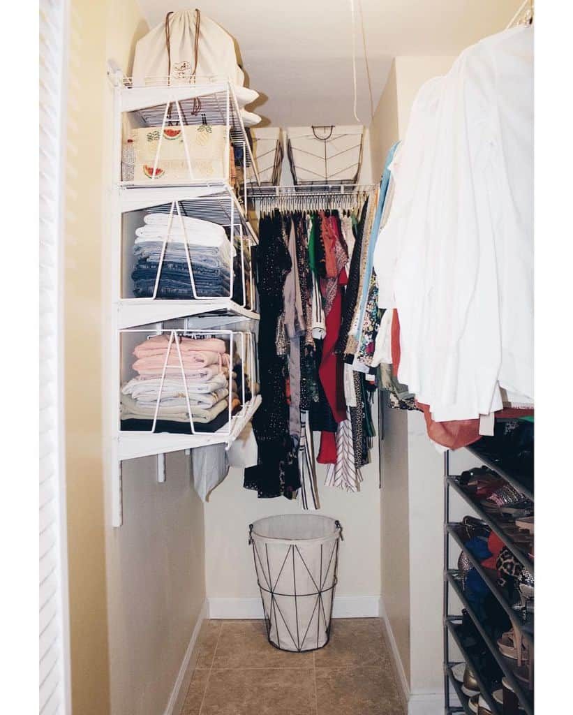 A neatly organized walk-in closet with clothes on hangers, folded items on shelves, and a laundry basket at the bottom