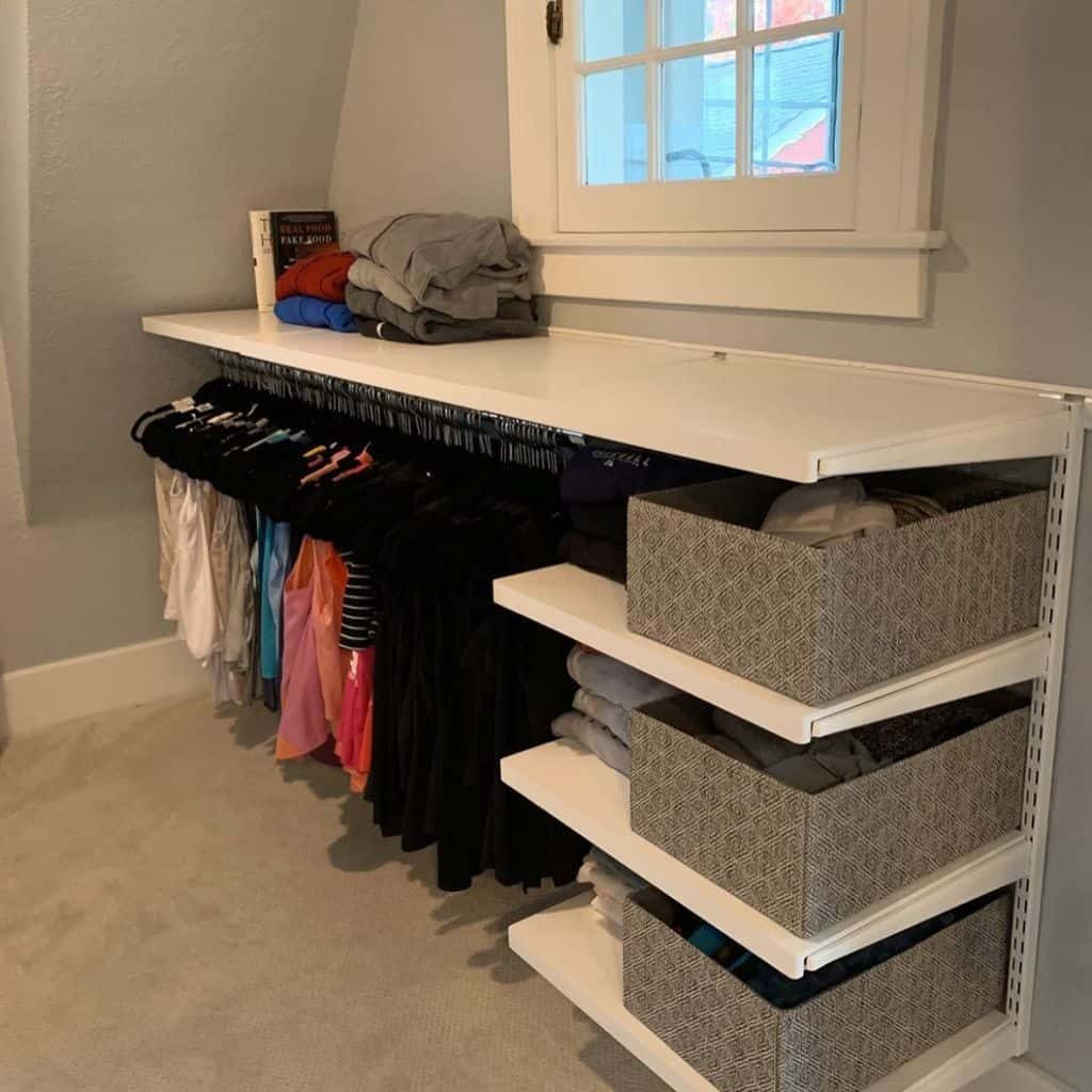 Neatly organized closet with clothes hanging below a shelf, folded shirts and baskets on shelves, and books on top