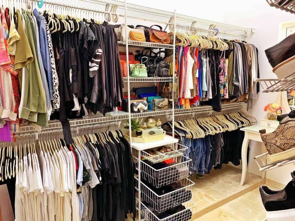 A neatly organized walk-in closet with clothes on hangers, shelves with bags, and drawers with accessories