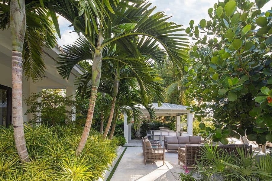 Luxurious outdoor cabana with cozy seating, lush tropical landscaping, and a modern pergola, creating a relaxing backyard retreat