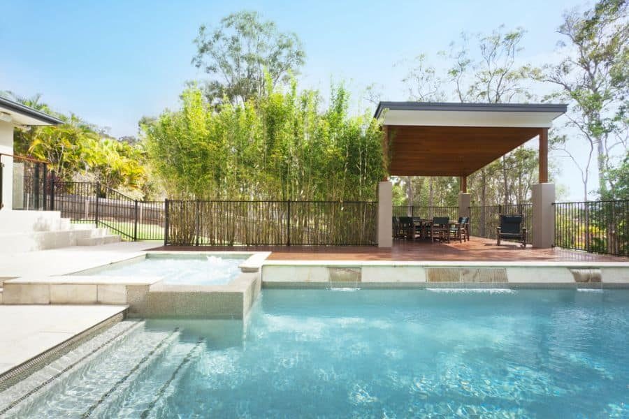 Modern poolside cabana with a wooden pergola, outdoor dining area, and lush bamboo backdrop, creating a private and stylish retreat