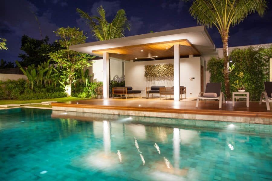 Elegant poolside cabana with a wooden deck, ambient lighting, and modern lounge seating, creating a serene nighttime retreat