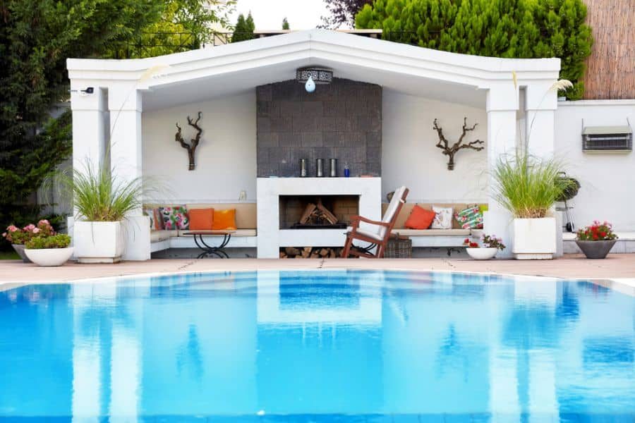 Charming poolside cabana with a cozy fireplace, built-in seating, and colorful cushions, creating a stylish and inviting outdoor retreat