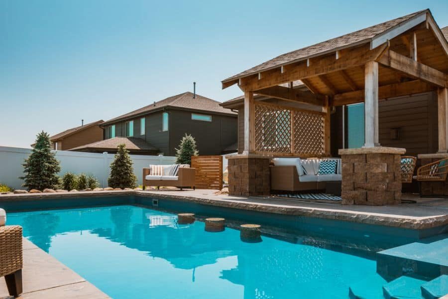 Rustic poolside cabana with wooden beams, stone pillars, and cozy seating, offering a shaded retreat beside a refreshing backyard pool