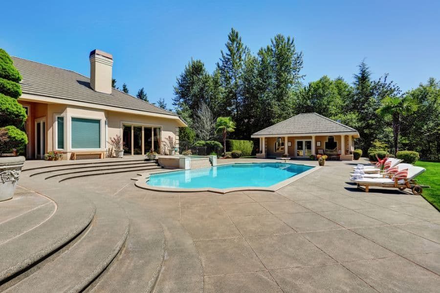 Spacious backyard with a luxurious pool, elegant pool house, and sun loungers, surrounded by lush greenery for a resort-style retreat