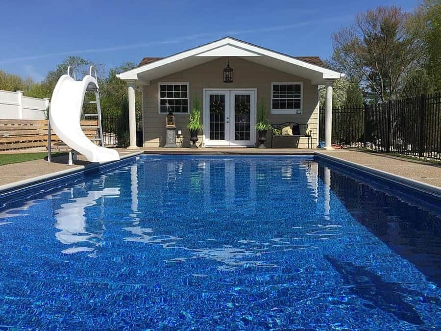 Charming pool house with a gabled roof, double doors, and a large swimming pool featuring a fun water slide, perfect for summer relaxation