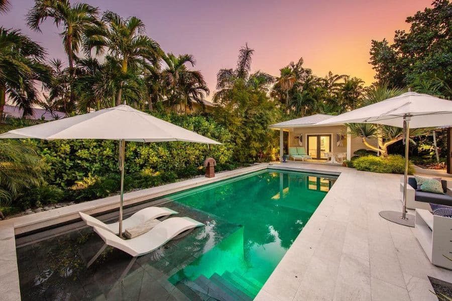 Serene tropical poolside retreat with a stylish cabana, lush greenery, sun loungers in the water, and umbrellas, set against a sunset sky