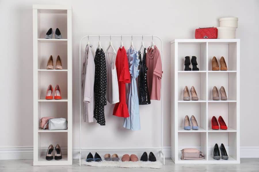 A tidy wardrobe with hanging clothes, shelves of shoes, bags, and a red purse on top; bright and organized closet space