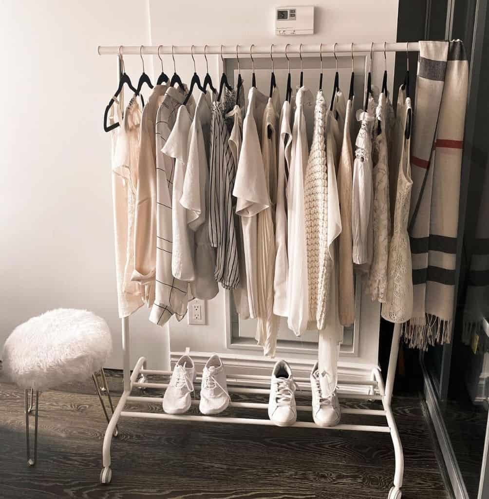 Stylish open wardrobe with a white clothing rack neatly displaying neutral-toned outfits and shoes, with a cozy stool nearby