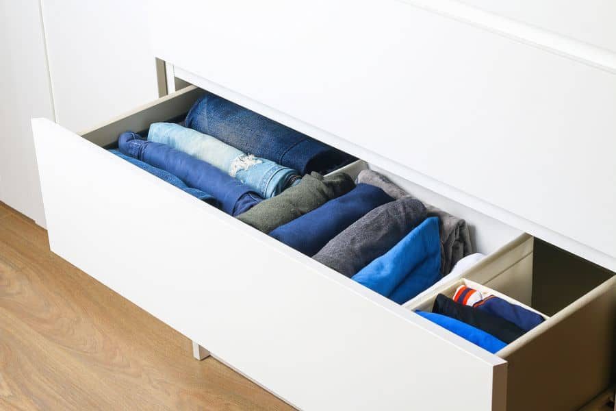 Open white drawer neatly organized with folded clothes in shades of blue and gray