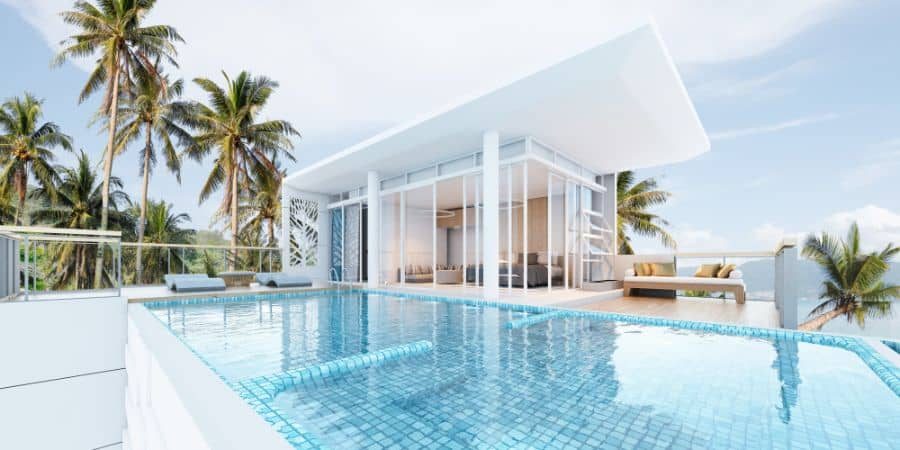 Modern glass pool house with a sleek white roof, infinity pool, and tropical palm tree backdrop, creating a luxurious resort-style escape