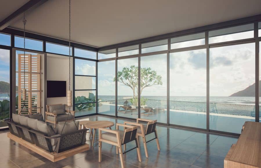 Modern glass pool house with floor-to-ceiling windows, a suspended sofa, and ocean views, creating a tranquil and stylish retreat