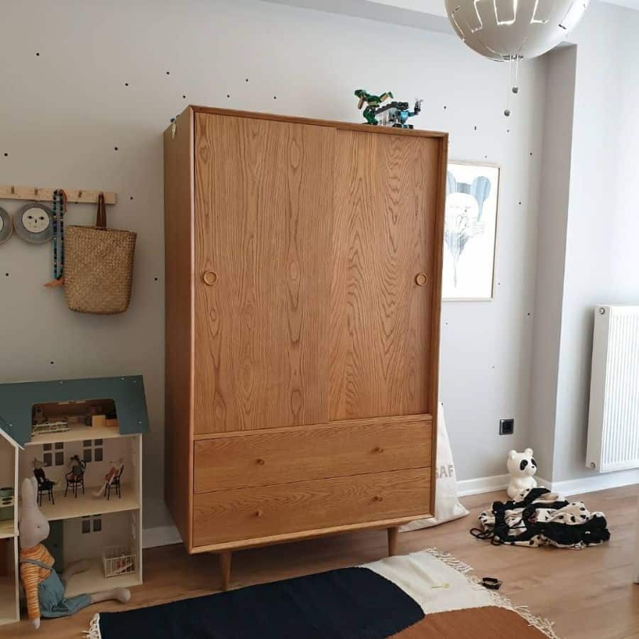 Modern kids' room with a wooden wardrobe, minimalist decor, dollhouse, woven storage basket, and playful wall details