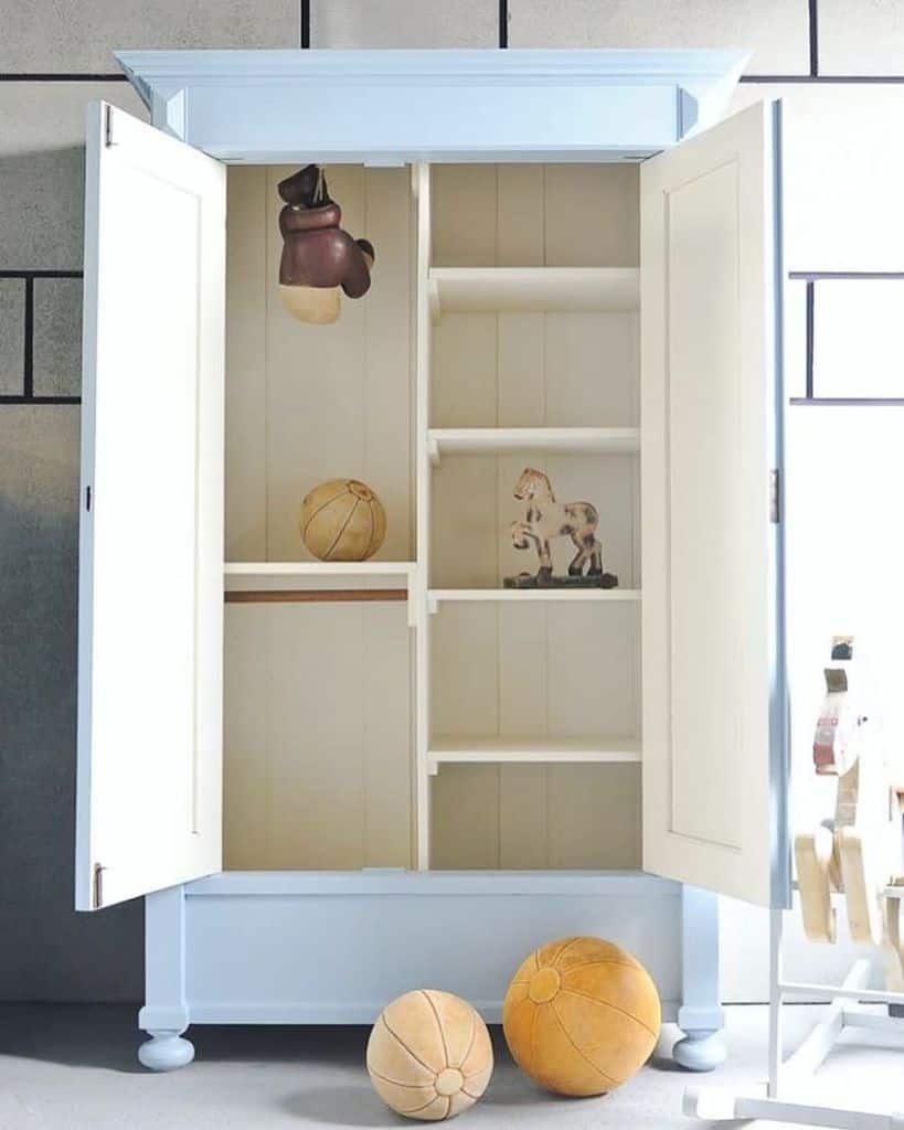 Vintage-style blue and white wardrobe in a kids' room, featuring open shelves, retro toys, boxing gloves, and antique wooden balls