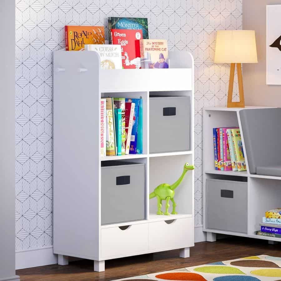 Modern kids' room with a white storage cabinet, colorful books, gray storage bins, a green dinosaur toy, and geometric wallpaper