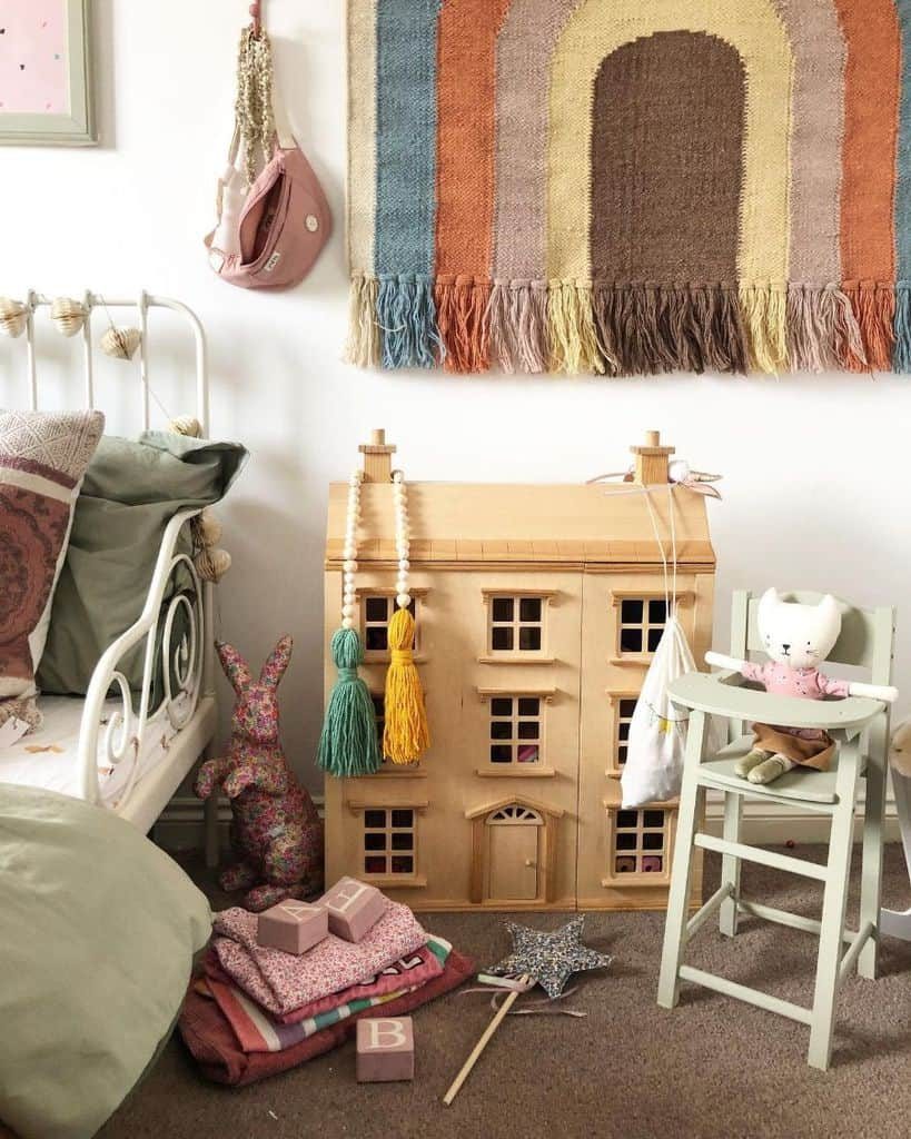 Cozy kids' room with a vintage-style dollhouse, pastel bedding, a rainbow wall tapestry, plush toys, and soft decorative accents