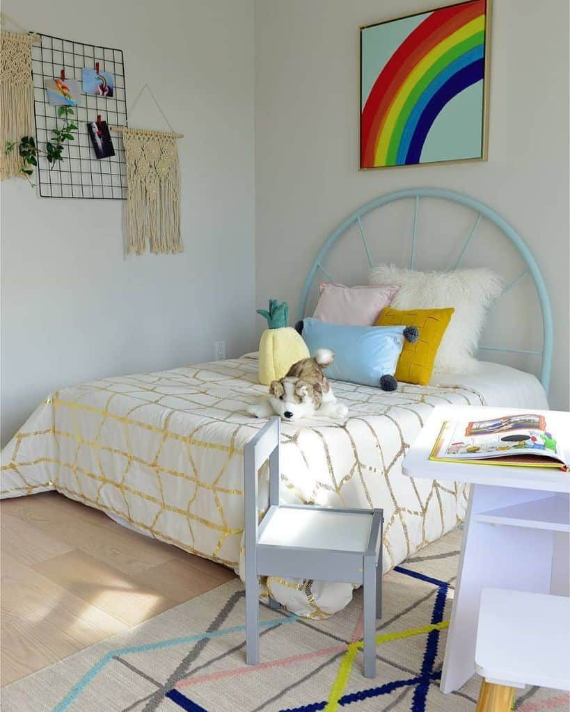 Bright and cheerful kids' room with a pastel blue bed frame, rainbow wall art, cozy pillows, macrame decor, and a small study table