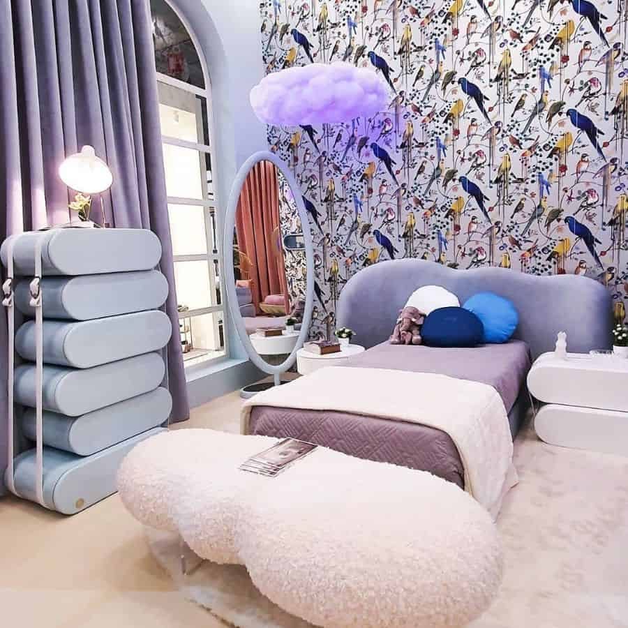 Whimsical kids' bedroom with a bird-patterned wallpaper, purple bedding, and a cloud-shaped light fixture, featuring a unique blue storage cabinet and a cozy white fuzzy bench