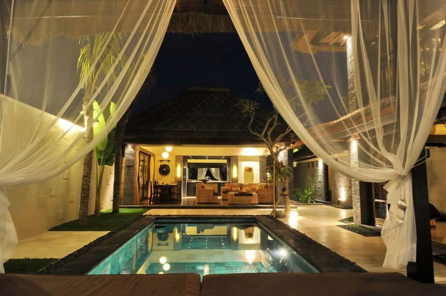 Tropical luxury pool house with sheer white curtains, warm ambient lighting, and a private plunge pool, creating a serene nighttime retreat