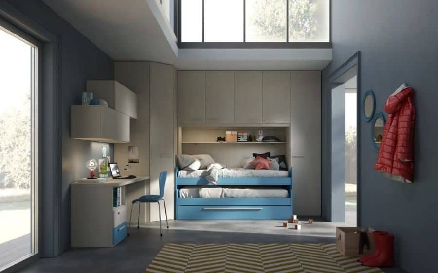 Modern kids' bedroom with a blue and gray color scheme, featuring a built-in bunk bed with storage drawers, a study desk with a blue chair, overhead cabinets, a geometric-patterned rug, and a high ceiling with large windows letting in natural light