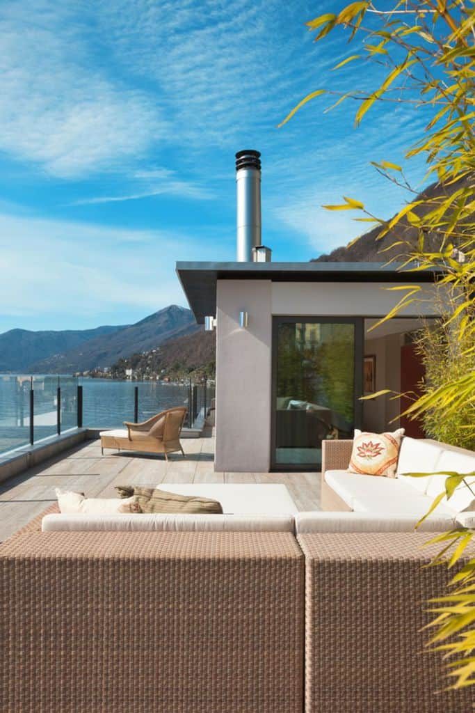 Modern pool house with a sleek terrace, wicker seating, and stunning lake and mountain views, creating a luxurious outdoor retreat