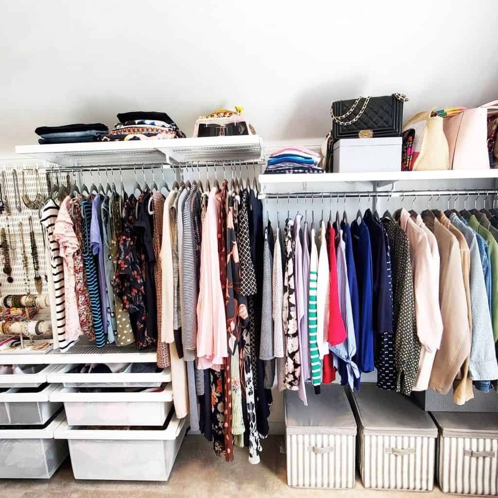 A neatly organized closet with clothing on hangers, folded items on shelves, and storage boxes below