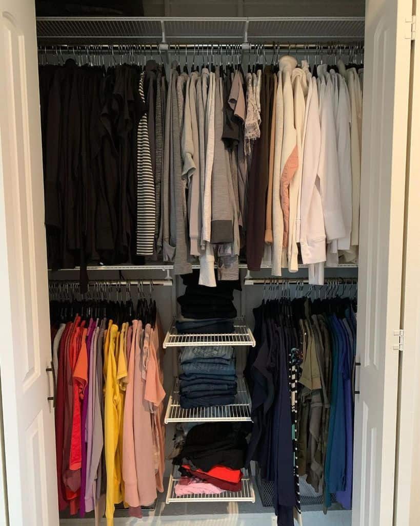 Organized closet with color-coordinated clothes on hangers and shelves, including shirts, pants, and folded jeans