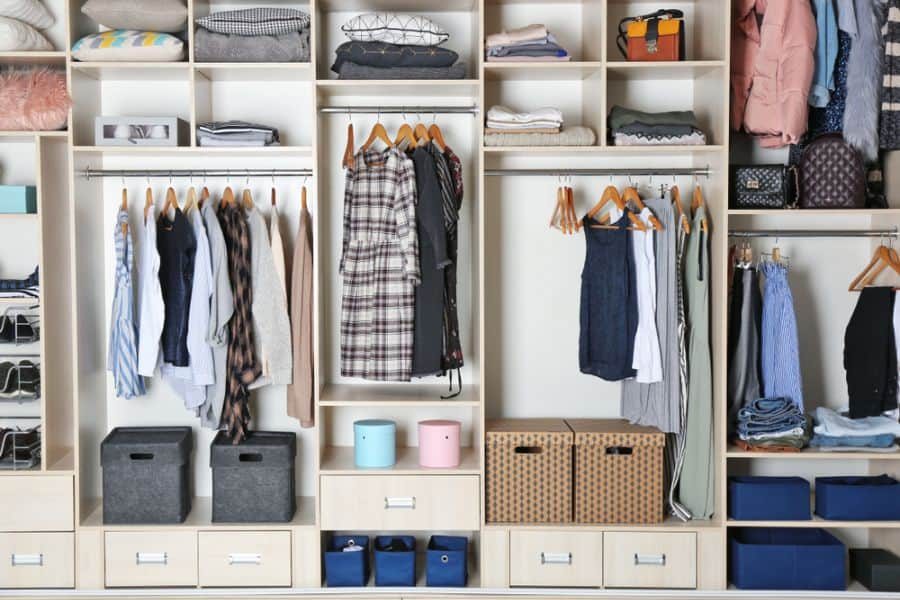 Organized closet with hanging clothes, folded items, storage boxes, and baskets; neutral tones and tidy arrangement