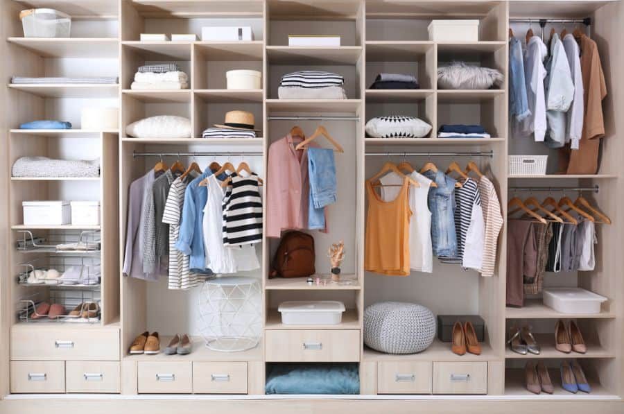 A neatly organized wooden wardrobe with clothes on hangers, folded items, shoes, and accessories in various compartments