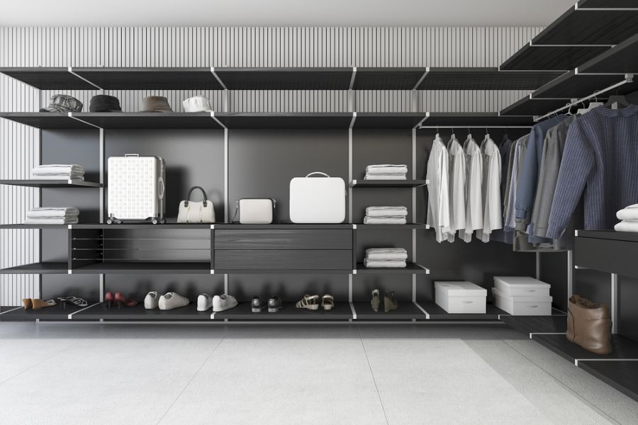 Minimalist walk-in closet with black shelves, white shirts, jackets, shoes, bags, and boxes neatly arranged on a textured wall