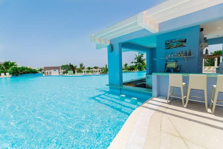 Resort-style swim-up pool bar with submerged seating, a shaded counter, and tropical surroundings, perfect for poolside relaxation