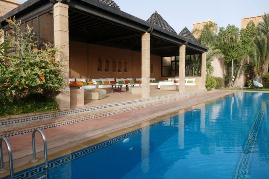 Elegant Moroccan-style pool pavilion with arched wall details, cozy built-in seating, and a tranquil blue-tiled swimming pool