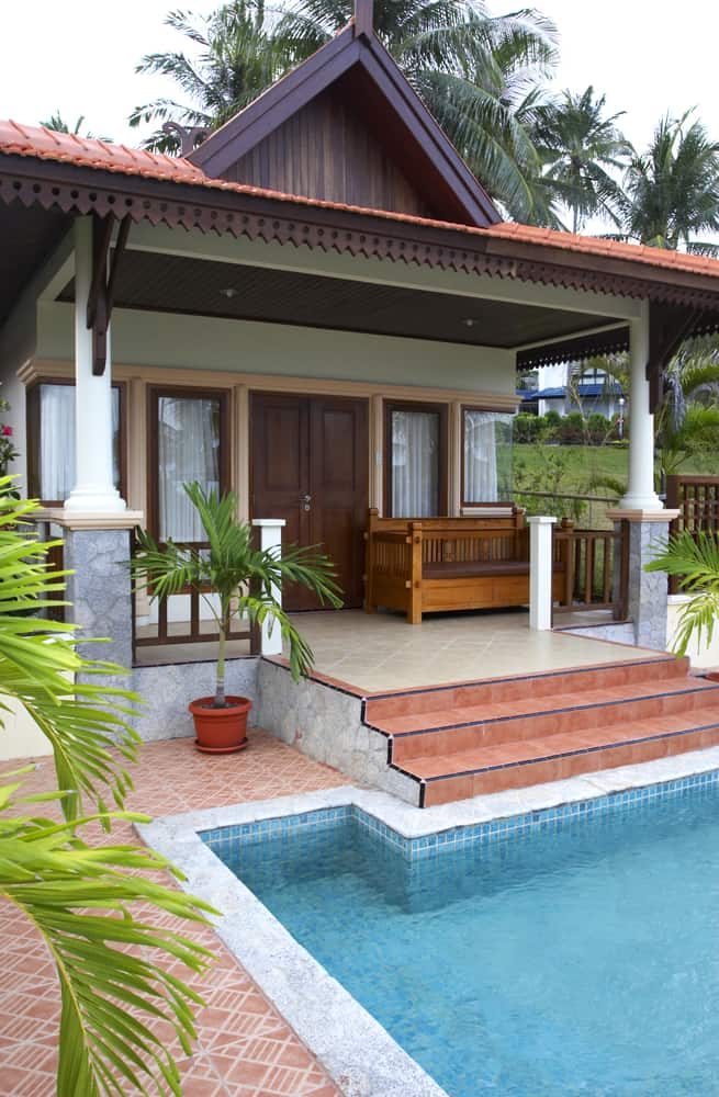 Enclosed pool houseTropical-style pool house with a red-tiled roof, wooden accents, and a small private pool, surrounded by lush greenery and palm trees