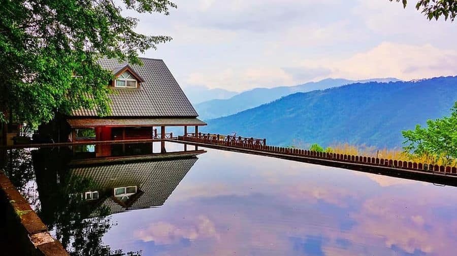 Scenic pool house with a sloped roof, overlooking a serene infinity pool that reflects the sky and mountains in a breathtaking landscape