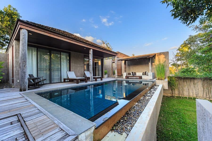 Modern tropical pool house with a sleek private pool, wooden deck, and open-air lounge, surrounded by lush greenery for a serene retreat