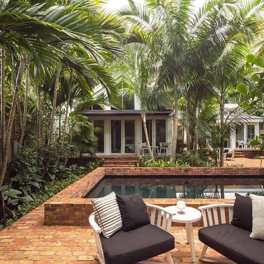 Serene tropical pool house with lush greenery, a brick-lined pool, and cozy outdoor seating, creating a private and relaxing retreat