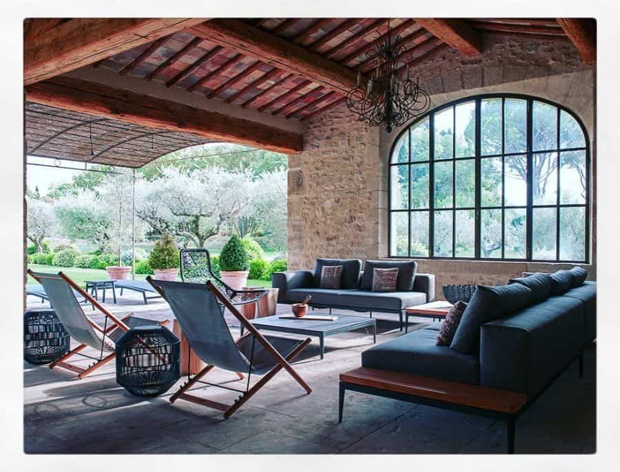 Rustic Mediterranean-style pool house with exposed stone walls, wooden beams, elegant arched windows, and cozy outdoor seating