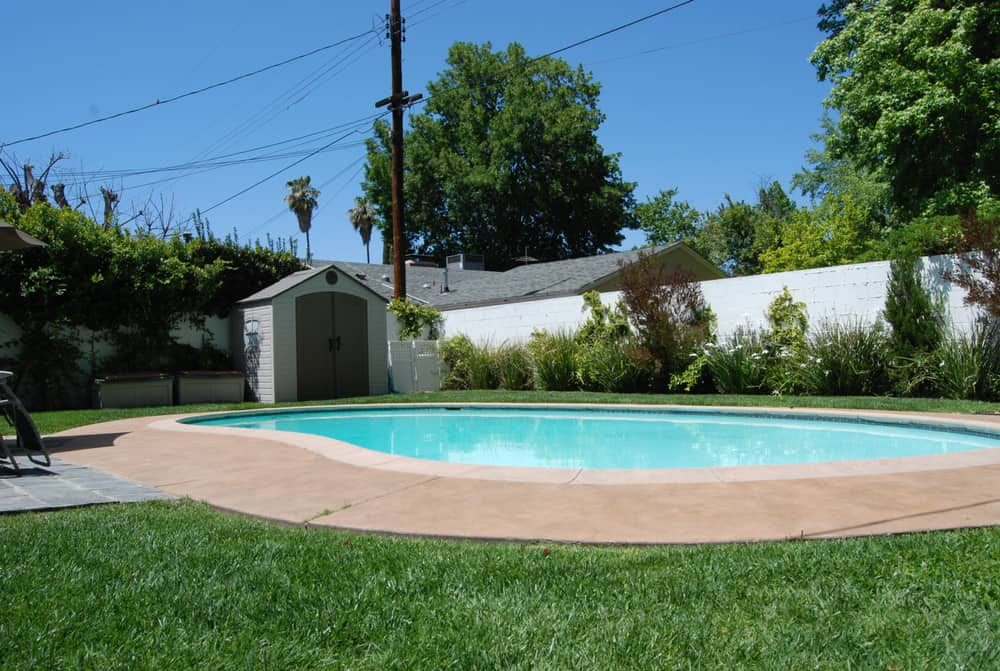 Cozy backyard pool with a compact storage shed, surrounded by lush greenery, a manicured lawn, and a private white fence for a serene retreat