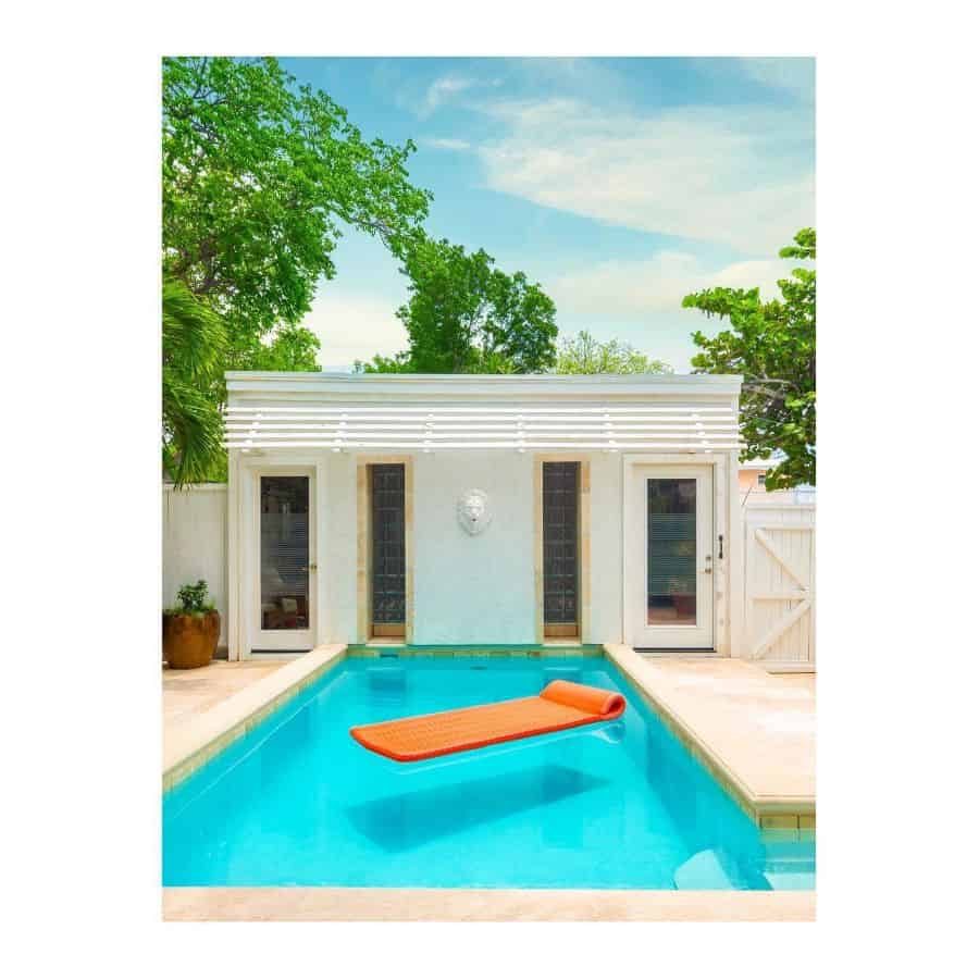 Stylish white pool house with glass-paneled doors, a compact turquoise pool, and an orange floating mat, creating a bright and inviting retreat