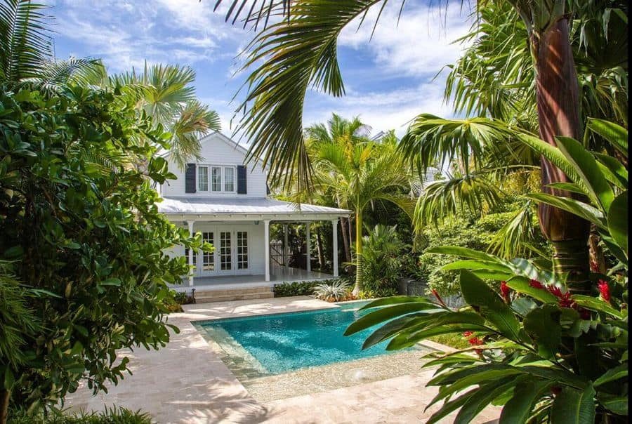 Tropical pool villa with lush greenery, a serene turquoise pool, and a charming white veranda, creating a private paradise retreat