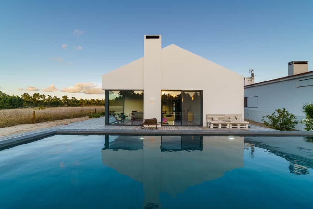 Minimalist modern pool villa with a sleek white facade, large glass doors, and a tranquil infinity pool reflecting the open countryside