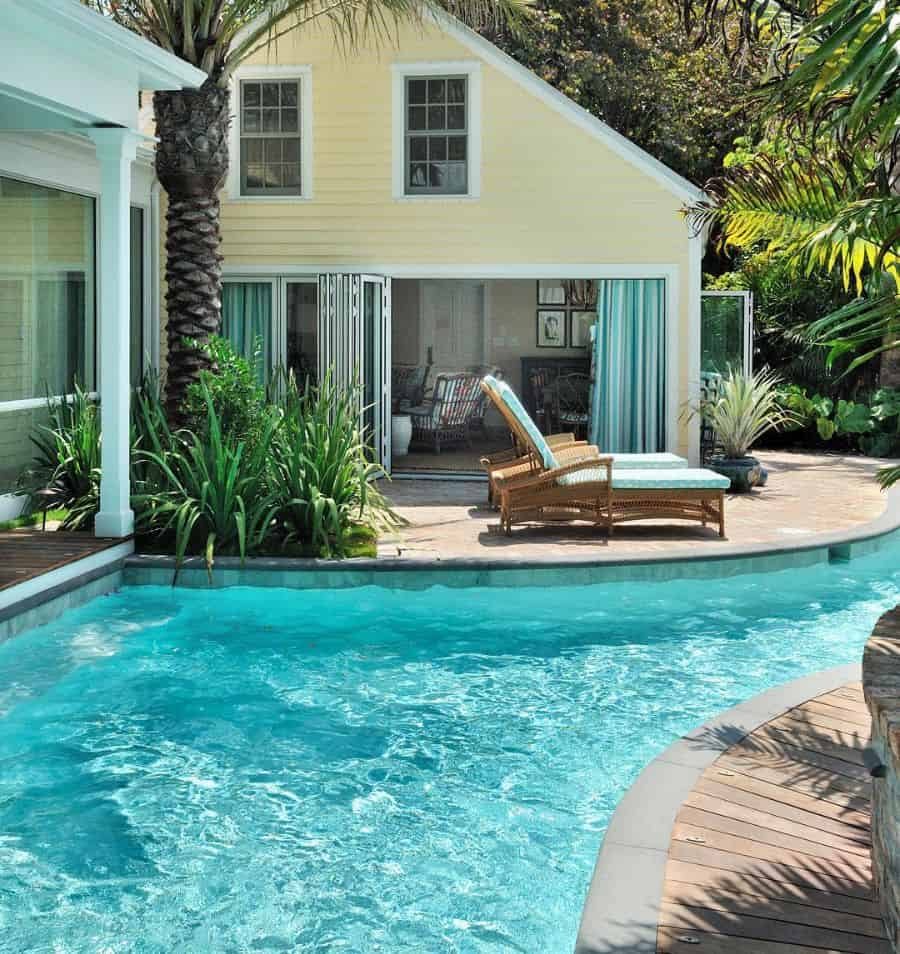 Charming tropical pool house with a soft yellow exterior, lush greenery, and a lagoon-style pool, creating a serene and inviting retreat